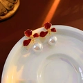 Dettaglio di orecchini a fiore in smalto rosso con perle su piatto in ceramica - Oro