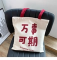 Detailed view of a white canvas tote bag with red handles and text on a black chair - Everything Can Be Expected