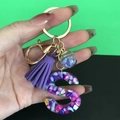 Hand holding resin letter S keychain with purple tassel and blue star glass ball charm - Letter S