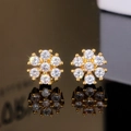 Vue détaillée de boucles d'oreilles fleurs dorées avec zircons étincelants sur fond noir - Doré
