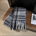Close-up of classic black and grey plaid scarf featuring long tassels on a wooden table - Baba Plaid Grey