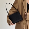 Detail of a black minimalist leather handbag styled with a khaki blazer on white background - Black