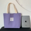 Borsa tote in tela viola con etichetta di cucciolo e manici color crema su sfondo bianco - Viola