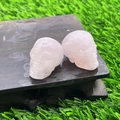 Two 2.8cm hand-carved pink rose quartz crystal mini skulls on a rustic wood base - Rose Quartz
