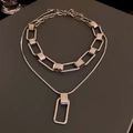 Detail of silver double-layered chain necklace with a rectangular pendant on grey surface - Double Layer Set / Silver