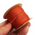 Close-up of 1mm red and gold twisted thread on a paper spool for DIY jewelry making - Orange Red