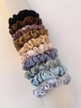 Détail de 12 chouchous en satin de couleurs variées empilés sur un rouleau blanc - Couleurs Dégradées Douces