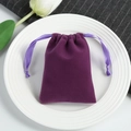 Close-up of purple velvet drawstring pouch on white ceramic plate with green leaves - Purple