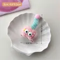 Pink plush hair clip with large eyes and blue spiral accents on a white tray - Pink Plush Hair Clip