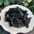 Macro shot of polished black obsidian long bar beads in a white shell dish with leaves - Obsidian