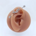 Makro-Detail des silbernen Industrial Barbell Ohrrings mit funkelnden Schmetterlingskristallen - Stil #6 Dreifach-Schmetterlingsreihe