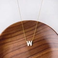 Collier doré avec pendentif lettre W en nacre blanche posé sur un support en bois - Lettre W
