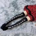 Close-up of black over-knee socks with white skull print against a plush carpet - One Size / Skull