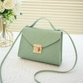 Minimalist light green woven handbag with gold square lock on an elegant white table - Green