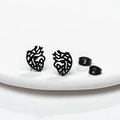 Macro shot of matte black hollow anatomical heart stud earrings on a white ceramic plate - Black