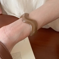 Primer plano de un brazalete de resina ámbar translúcida con diseño ondulado en la muñeca - Ámbar Caramelo (Café Oscuro) / 【atributos Del Producto】este Producto Es Una 【pulsera/brazalete Con Forma De Onda】de Un Color 【marrón Ámbar/caramelo】semitransparente Y El Material Parece Ser 【resina O Acrílico】.