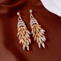 Dettaglio di orecchini a nappa in cristallo champagne su un lussuoso tessuto di seta marrone - Stile Nappa a Piuma Oro Champagne