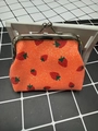 Close-up of an orange strawberry print coin purse with a glitter finish and silver metal clasp - Orange