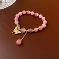 Gros plan d'un bracelet en perles œil-de-chat avec pendentif papillon doré et cristaux - Rose