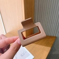 Close-up of a matte light brown square hair claw clip held in hand for hairstyling - Coffee