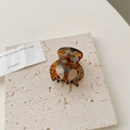Vue macro d'une pince à cheveux en acétate léopard sur une plaque de pierre beige - Écaille de Tortue Foncée