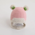 Detailed close-up of pink knitted baby hat with white faux fur balls and green frog patch - One Size (Recommended 2-8 Years Old) / Pink