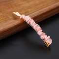 Macro shot of natural pink crystal chips on a golden metal hairpin against wood - Pink Opal Gold