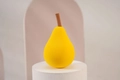Pear-shaped yellow makeup sponge with brown stem on a white pedestal in minimalist setting - Yellow Pear with Stem