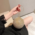 Bolso de fiesta esférico dorado con pulsera de pedrería sostenido por una modelo - Dorado