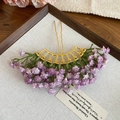 Dettaglio degli eleganti fiori di gipsofila viola su una forcina per capelli dorata a U - Viola