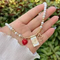Dettaglio della collana di perle placcata oro 18K con cuore rosso, medaglia e croce - Lettera Bianca B