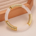 Dettaglio del bracciale a maglie intrecciate in acrilico e metallo dorato su legno - Bianco