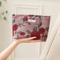 Pink canvas cosmetic bag with red rose jacquard pattern held in hand for display - Peony