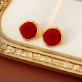 Detail of red flocked geometric earrings with gold textured frames on soft fabric - Red