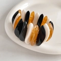 Detailed macro view of black, white, and amber resin geometric bangles on ceramic tray - Pebble Style Black White & Amber Splicing
