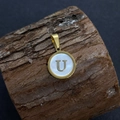 Golden round pendant with letter U in white seashell inlay on a wood texture background - Letter U / 17x20mm