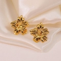 Polished gold flower stud earrings elegantly placed on soft beige silk background - Gold