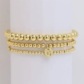 Set di tre braccialetti con perline dorate e ciondolo lettera G su espositore bianco - Lettera G