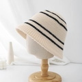Detalle de gorro de punto beige con rayas negras en un soporte de madera elegante - Beige con rayas negras
