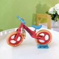 Miniature red and blue balance bike keychain toy presented on a blue display stand - Bicycle Keychain - Orange