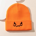 Detailed view of bright orange knit beanie featuring black embroidered pumpkin face - Orange
