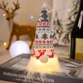 Close-up of glowing Christmas gnome ornament with warm LED light on decorative books - Style F (Red Grey White Geometric)