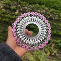 Macro shot of silver circular metal ornament with radial patterns and pink gemstones - Bright Silver Rose Red