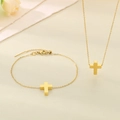 Dettaglio del set di collana e bracciale con ciondolo a croce dorata su tessuto beige - Collana d'Oro (KS223544-Z)