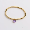 Close-up of golden beaded stretch bracelet with purple heart enamel charm on white background - Purple