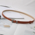 Schmaler brauner PU-Ledergürtel mit gravierter Metallschnalle auf einem Modemagazin - Khaki