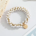 Detail of handmade pearl hair tie with gold woven threads and a round metal logo tag - Pure Pearl Style