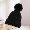 Close-up of black cable knit beanie with large faux fur pompom on a display stand - Black