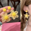 Detalle de pendientes de flores de rafia amarillos hechos a mano en mano y puestos. - Amarillo