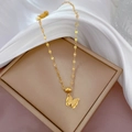 Dettaglio di una collana con ciondolo a farfalla dorata su una scatola beige e seta - Oro (K232)